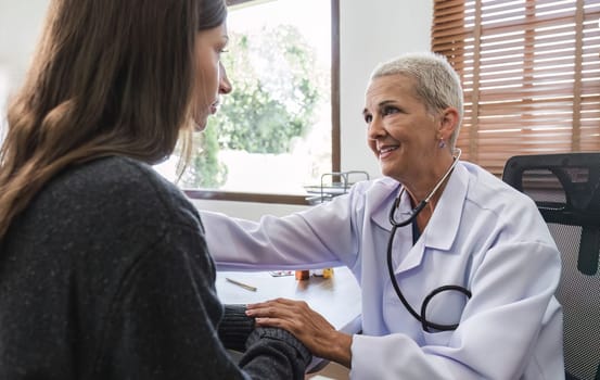 Elderly female doctor in white coat talking with beautiful young patient in clinic, giving advice on heart disease treatment and health care and medicine, medicine concept.