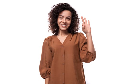 young successful pretty caucasian woman with curly black hair is dressed in a brown shirt on a white background.
