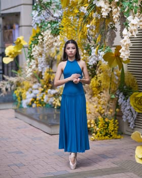 Beautiful Asian ballerina posing against the backdrop of a building decorated with flowers