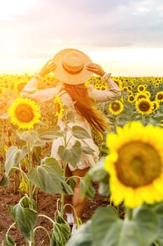 Woman sunflower field. Happy girl in blue dress and straw hat posing in a vast field of sunflowers at sunset. Summer time