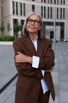 a slender gray-haired business woman of mature years is dressed in an elegant brown suit on a city street.