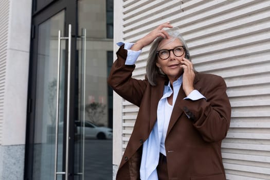 well-groomed business woman of mature years dressed in elegant brown speaks on the phone while waiting for a business meeting.