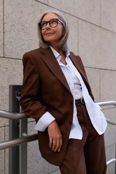 close-up portrait of a charming slim mature woman with gray hair in a stylish suit on the street.