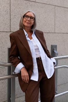 business portrait of a confident successful 60 year old gray-haired lady in glasses wearing a brown jacket.