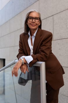 portrait of a slender cute gray-haired entrepreneur woman of mature years in a brown suit on the background of the building.