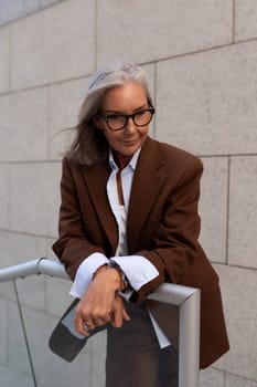 close-up of a slender well-groomed pretty gray-haired business woman pensioner standing on the porch of the building.