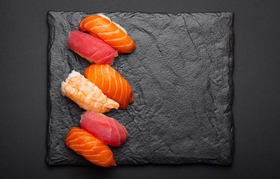 Traditional Japanese sushi top view on dark black rustic slate. Sushi with salmon, tuna and shrimp, space for text, template for Japanese restaurant menu