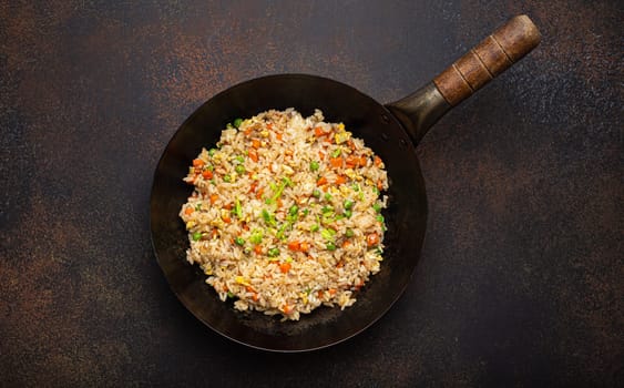 Authentic Chinese and Asian fried rice with egg and vegetables in wok top view on rustic concrete table background. Traditional dish of China