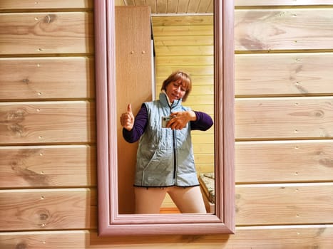 Middle-aged woman using smartphone for selfie and blogging. Female blogger poses in a photo. The girl admires herself in the mirror