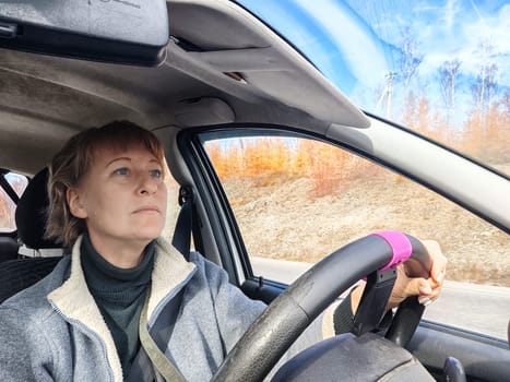 Portrait of female driver in solo journey. Adult mature woman holding steering wheel and looking through windscreen in travel by vehicle on vacation. Lady girl who is owner or rent car for travel