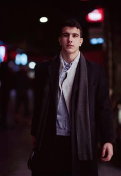 Smiling Meedle Eastern man walking down street near modern office building, freelancer businessman looking away holding mobile phone on busy city street at night