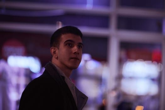 Smiling Meedle Eastern man walking down street near modern office building, freelancer businessman looking away holding mobile phone on busy city street at night