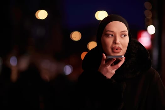 Beautiful and elegant European Muslim Hijabi Business Lady checking her phone and social media on urban city street at night