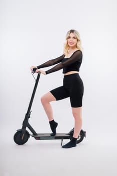 Beautiful emotional young female in a sport clothes on electric scooter on red and white background