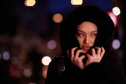 Muslim woman walking on an urban city street on a cold winter night wearing hijab with bokeh city lights in the background