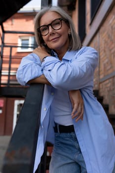 confident mature old woman with gray hair dressed stylishly walks around the city and stopped on the stairs.