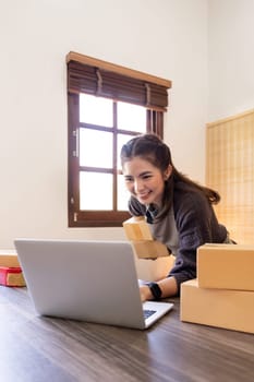 Startup SME small business entrepreneur of freelance Asian woman using laptop and box to receive and review order online to prepare to pack sell to customers, online sme business ideas.