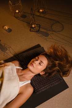 A woman lies on the floor covered with a blanket with her eyes closed and relaxes after a workout , shavasana pose.