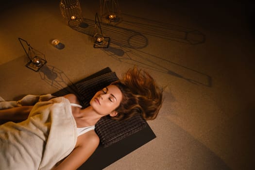 A woman lies on the floor covered with a blanket with her eyes closed and relaxes after a workout , shavasana pose.