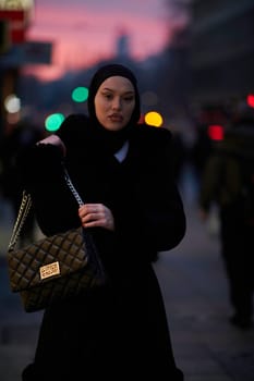 Muslim woman walking on an urban city street on a cold winter night wearing hijab with bokeh city lights in the background