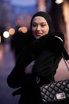 Muslim woman walking on an urban city street on a cold winter night wearing hijab with bokeh city lights in the background