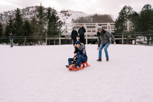 Dad pushes mom with a child on a sled going down a hill. High quality photo