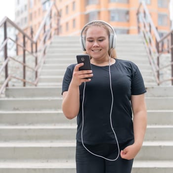A fat young woman goes down the stairs and listens to music on a smartphone