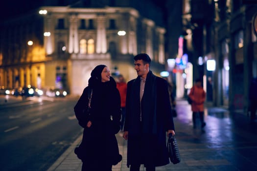 Happy multicultural business couple walking together outdoors in an urban city street at night near a jewelry shopping store window. Successful Arab businessman and European Muslim woman.