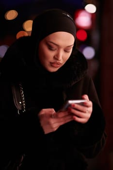 Beautiful and elegant European Muslim Hijabi Business Lady checking her phone and social media on urban city street at night