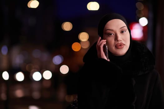 Beautiful and elegant European Muslim Hijabi Business Lady checking her phone and social media on urban city street at night