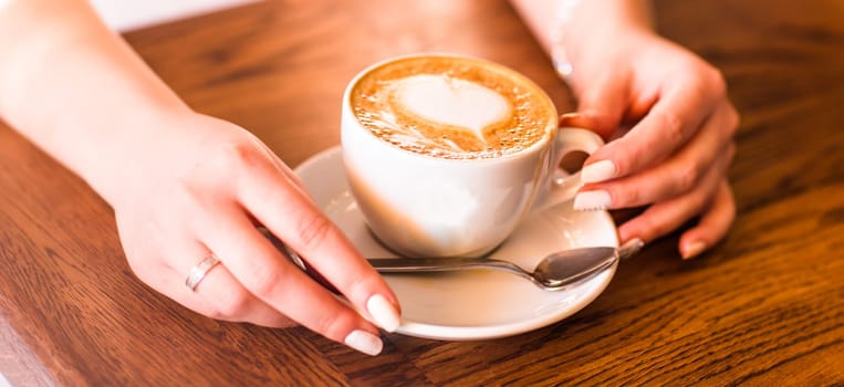 woman holding hot cup of coffee, with heart shape.