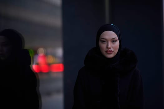 Muslim woman walking on an urban city street on a cold winter night wearing hijab with bokeh city lights in the background