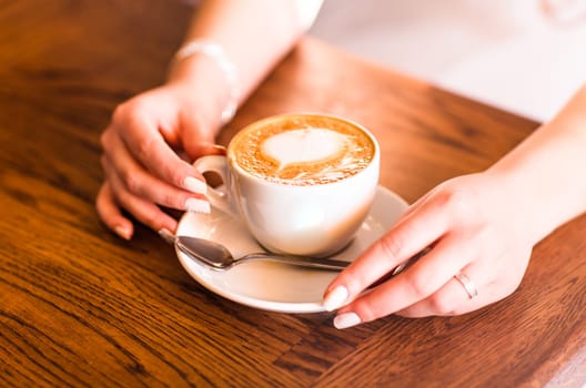 woman holding hot cup of coffee, with heart shape.