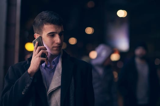 Smiling Meedle Eastern man walking down street near modern office building, freelancer businessman looking away holding mobile phone on busy city street at night