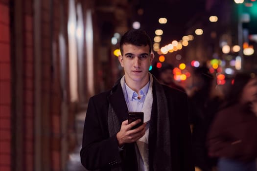 Smiling Meedle Eastern man walking down street near modern office building, freelancer businessman looking away holding mobile phone on busy city street at night