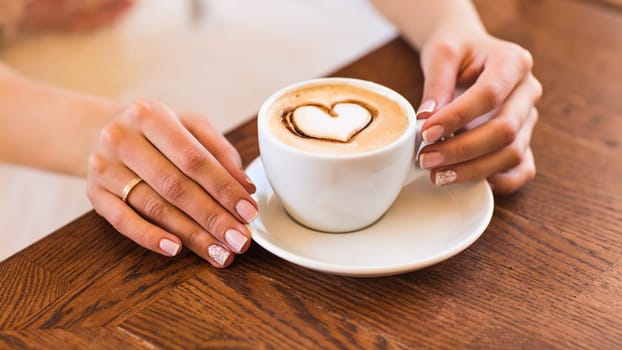 woman holding hot cup of coffee, with heart shape.