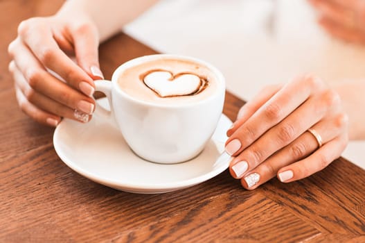 woman holding hot cup of coffee, with heart shape.