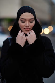 Muslim woman walking on an urban city street on a cold winter night wearing hijab with bokeh city lights in the background