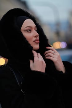 Muslim woman walking on an urban city street on a cold winter night wearing hijab with bokeh city lights in the background