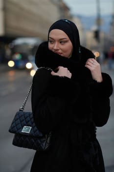 Muslim woman walking on an urban city street on a cold winter night wearing hijab with bokeh city lights in the background