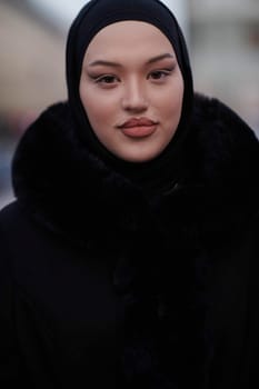 Muslim woman walking on an urban city street on a cold winter night wearing hijab with bokeh city lights in the background