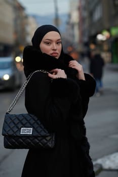 Muslim woman walking on an urban city street on a cold winter night wearing hijab with bokeh city lights in the background