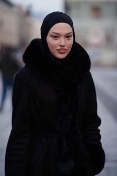 Muslim woman walking on an urban city street on a cold winter night wearing hijab with bokeh city lights in the background