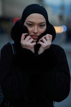 Muslim woman walking on an urban city street on a cold winter night wearing hijab with bokeh city lights in the background