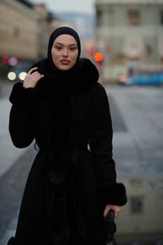 Muslim woman walking on an urban city street on a cold winter night wearing hijab with bokeh city lights in the background