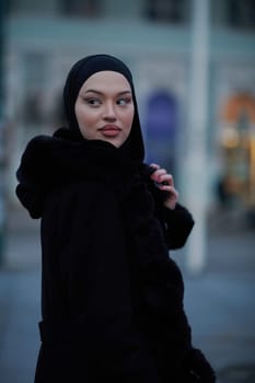 Muslim woman walking on an urban city street on a cold winter night wearing hijab with bokeh city lights in the background