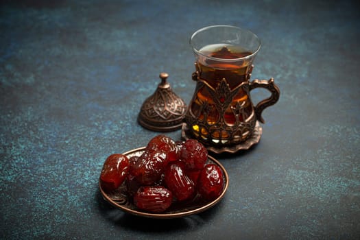 Breaking fasting with dried dates during Ramadan Kareem, Iftar meal with dates and Arab tea in traditional glass, angle view on rustic blue background. Muslim feast.