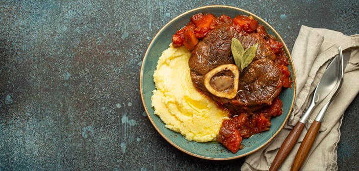 Traditional Italian dish Ossobuco all Milanese made with cut veal shank meat with vegetable tomato sauce served with corn polenta on ceramic plate top view on rustic stone background, copy space.