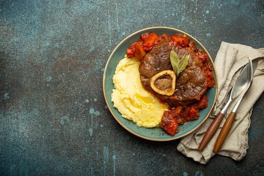 Traditional Italian dish Ossobuco all Milanese made with cut veal shank meat with vegetable tomato sauce served with corn polenta on ceramic plate top view on rustic stone background, copy space.