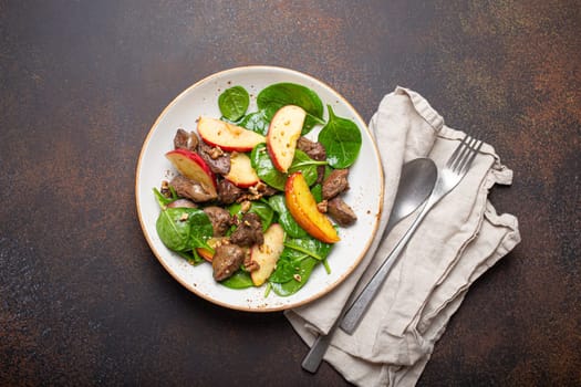 Healthy Salad with Iron Rich Ingredients Chicken Liver, Apples, Fresh Spinach and Walnuts on White Ceramic Plate, Dark Brown Rustic Stone Background Top View.